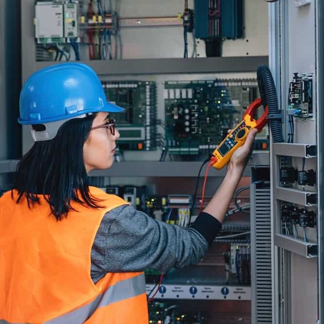 woman industrial service electrician female engineer wearing protective vest and helmet testing electric voltage